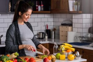 Una mujer embarazada corta comida saludable porque sigue una dieta para embarazadas.