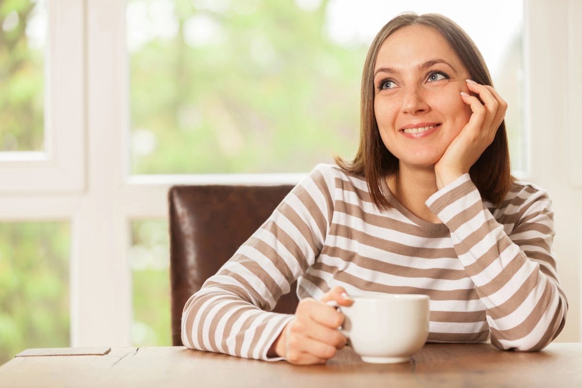 Una mujer sentada tomando una taza con la mano piensa qué tipo de inositol es mejor para ella y su salud.