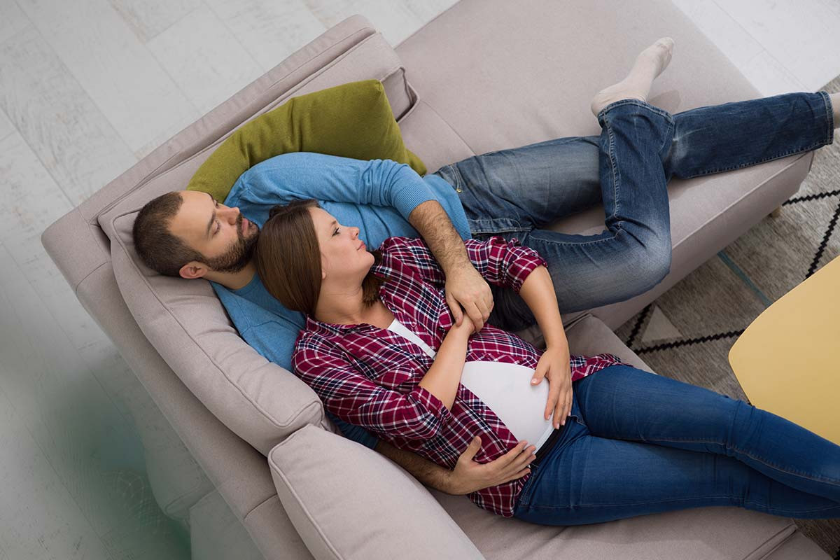 Una pareja acostados abrazados en un sofá muestran la importancia de la preparación masculina para el embarazo.