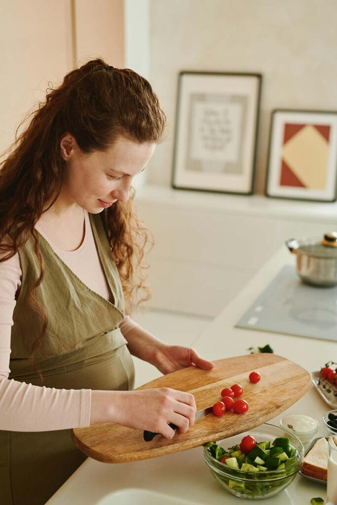 Mujer embarazada preparando una ensalada como parte de su alimentación equilibrada complementada con suplementos durante el embarazo.