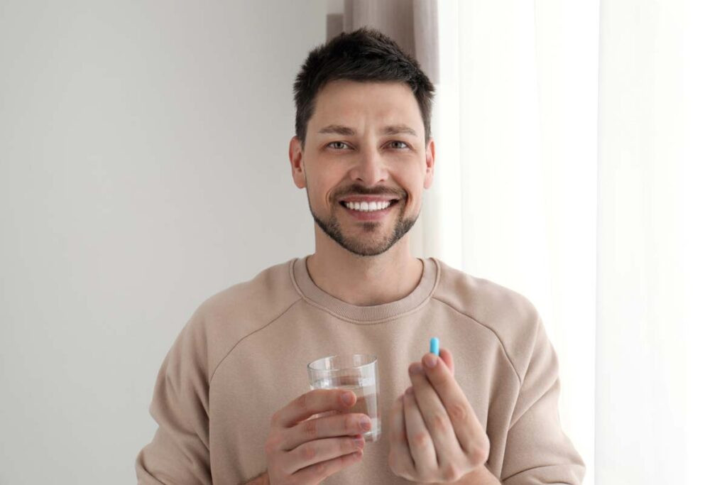 Hombre joven feliz y saludable sosteniendo un vaso de agua y un suplemento de zinc para la fertilidad masculina.